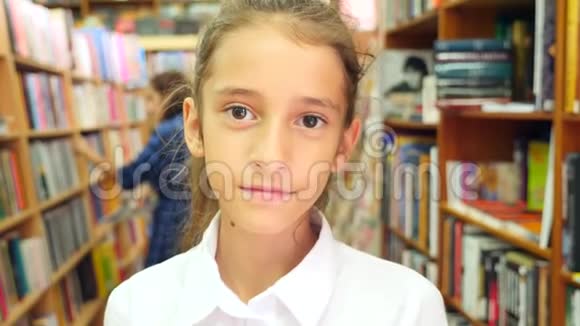 一幅812岁女孩站在图书馆的肖像背景中书架的书架4k慢视频的预览图