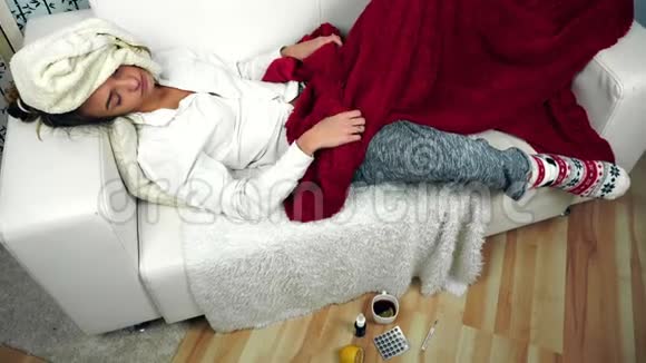 生病的女人躺在沙发上的毯子下面地板上放着药物视频的预览图