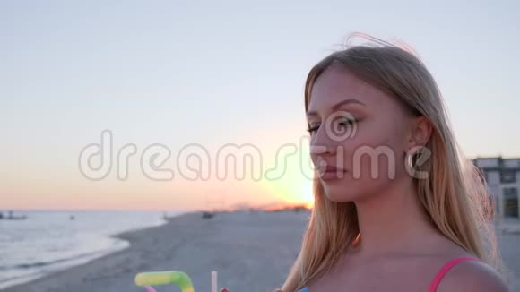 肖像女孩看着远处的海洋喝着彩色鸡尾酒视频的预览图