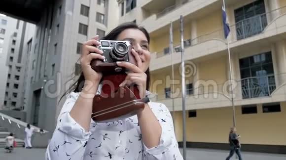 一个年轻快乐的女人留着长发用旧的手动相机拍摄现代建筑的照片视频的预览图
