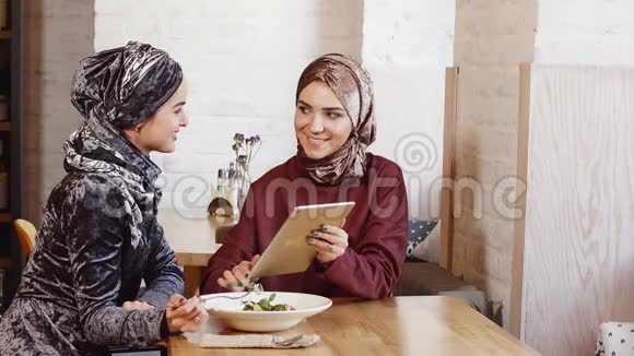 两个漂亮的穆斯林女人在咖啡馆里用平板电脑视频的预览图