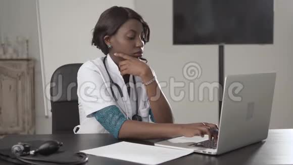 颇具吸引力的非洲医生在电话中用笔记本电脑工作在内阁医院写诊断报告视频的预览图