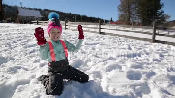 快乐的小女孩在雪地里玩坐在地上在空中扔雪花阳光明媚的冬季视频的预览图