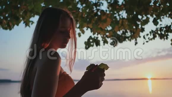一个年轻的女孩在湖边日落时触摸花瓣视频的预览图