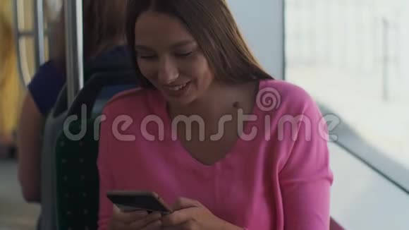 年轻快乐的女人在旅行中坐在靠近窗户的公共交通工具上使用智能手机视频的预览图