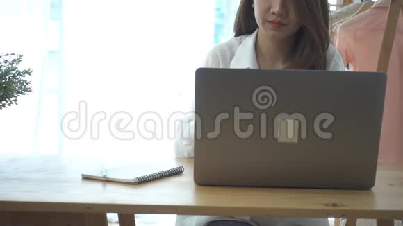 慢动作美丽的年轻微笑的亚洲妇女工作在笔记本电脑而坐在客厅在家里视频的预览图