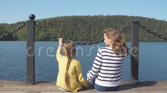 母亲和女儿坐在码头温暖的秋日视频的预览图