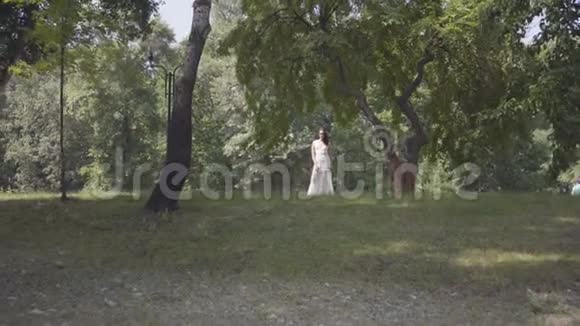 一个可爱的小女孩一头长长的黑发穿着一件白色的夏装站在树枝下视频的预览图