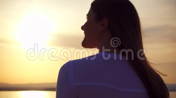 在湖上日落时微笑的年轻女子的剪影女性在黄金时刻缓慢运动视频的预览图