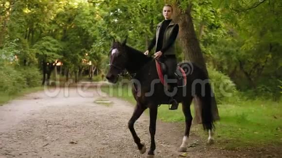 漂亮的女人在公园里骑着漂亮的棕色马美丽的女骑手坐在马鞍上走路视频的预览图