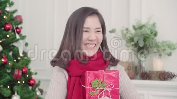 圣诞佳节快乐的年轻亚洲女人在家的客厅里捧着圣诞礼物微笑着拍照视频的预览图