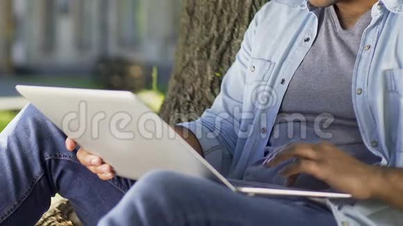 学生在他的笔记本电脑上写报告坐在大学校园的树下视频的预览图