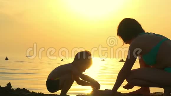 母子在沙滩上玩耍妈妈和孩子在大海的背景下建造一座沙堡视频的预览图