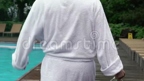 穿着浴袍的年轻人拿着一瓶香槟在泳池边散步视频的预览图