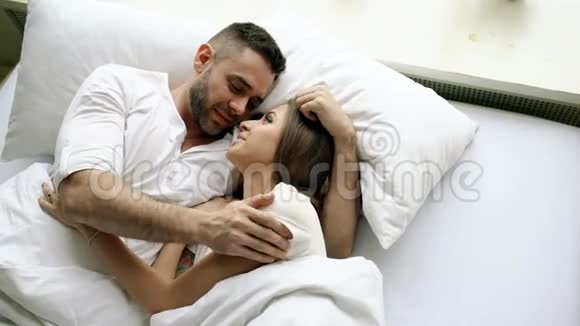 年轻美丽而有爱心的一对夫妇在早上醒来时交谈并拥抱在床上迷人的男人的俯视图视频的预览图