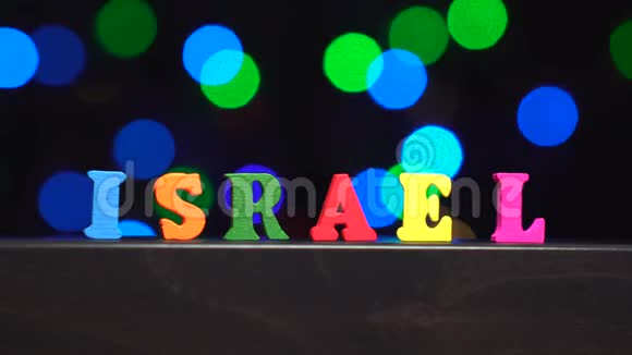 色彩斑斓的词以色列由多种颜色的木制字母在抽象模糊的灯光前背景视频的预览图