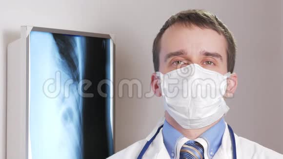 一个戴着面罩的年轻医生看着相机微笑背景下悬挂患者x线衬衫视频的预览图