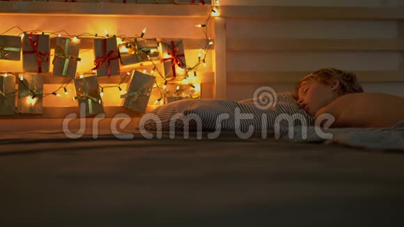 一个小男孩睡在他的床上他的床背上有一盏圣诞灯照着他的圣诞日历视频的预览图