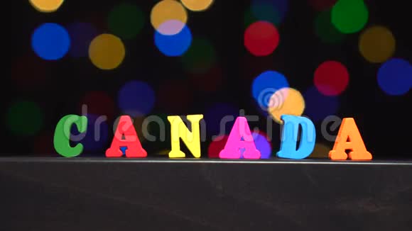 色彩斑斓的单词加拿大由多种颜色的木制字母在抽象模糊的灯光前背景视频的预览图