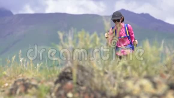 年轻女子带着蓝色背包徒步旅行带着绿草的美丽的山视频的预览图