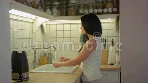 年轻女子用肥皂洗脏盘子和厨房里的人说话视频的预览图
