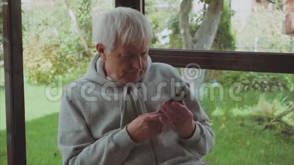 老人白发苍苍坐在花园里的阳台上使用智能手机视频的预览图