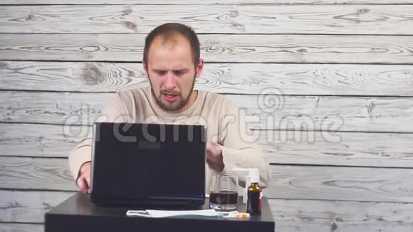 生病的胡子男咳嗽坐在工作场所用电脑视频的预览图