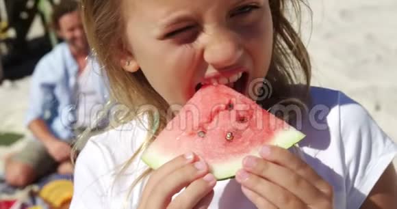 女孩吃西瓜而父亲坐在海滩的背景下视频的预览图