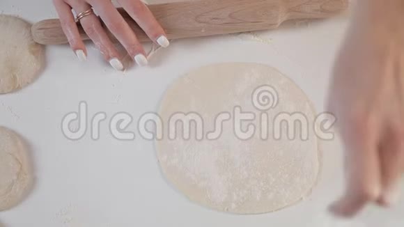 女面包师用擀面杖在木桌和面粉上的配料背景上滚动面团视频的预览图