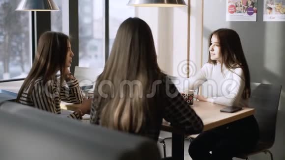咖啡馆里的朋友女孩们在咖啡馆里喝咖啡三个女朋友坐在咖啡馆的一张桌子旁视频的预览图