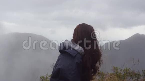 女旅行者坐在美丽的峡谷边缘看着大自然穿着雨衣的年轻女游客视频的预览图
