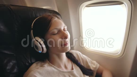 年轻女子戴着无线耳机在飞机上听音乐微笑视频的预览图