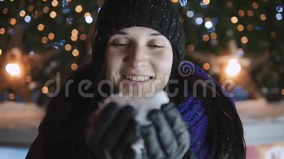年轻女子站在圣诞树旁的手中吹着雪花新年快乐概念户外视频的预览图