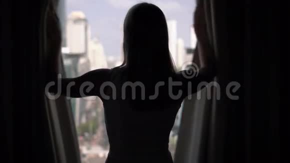 女人揭开窗帘和看窗外的剪影城外摩天大楼景观视频的预览图