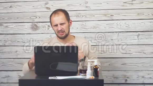 生病的胡子男咳嗽坐在工作场所用电脑视频的预览图