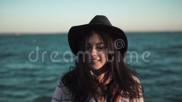 海洋背景上可爱女孩特写的肖像穿着秋装戴帽子的年轻女子在镜头前摆姿势微笑视频的预览图