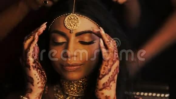 迷人的印度新娘把她娇嫩的手指放在太阳穴后面而女人则准备好她的头发视频的预览图