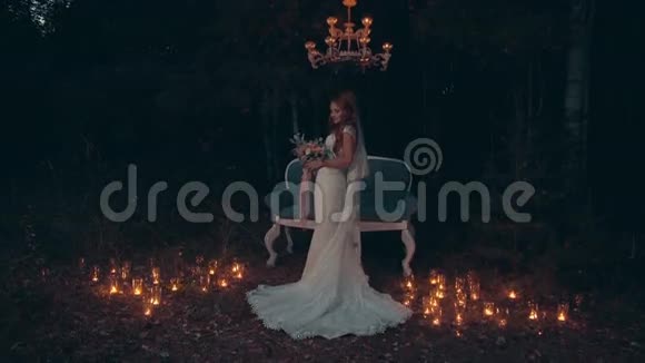 新娘拿着花束站在黑暗森林的沙发前点燃蜡烛视频的预览图