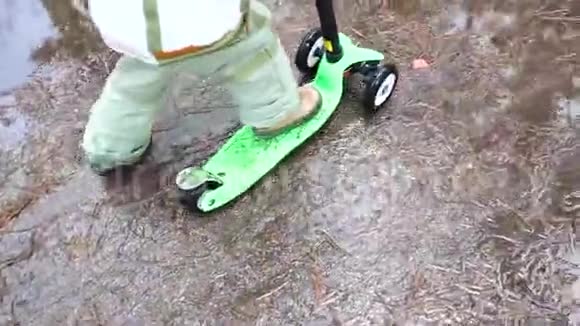早春孩子在公园里骑滑板车融化的雪雪和水坑上的沥青户外运动视频的预览图