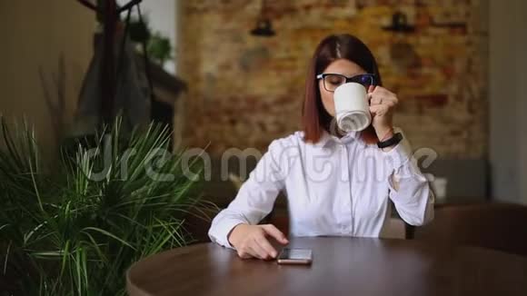 带眼镜的浅黑色混血儿喝着芬芳的咖啡用手机拨通短信看着视频的预览图