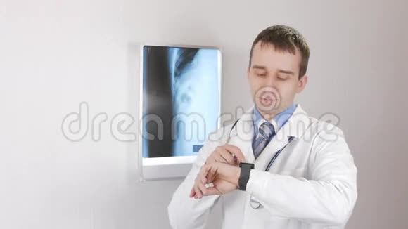 年轻的男医生检查智能手表上的信息白色墙壁和X光透视器肋骨和肋骨在上面视频的预览图