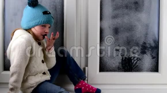 小女孩坐在冰冻的窗户后面的窗台上低自由度视频的预览图