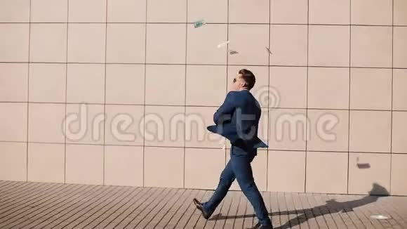 年轻快乐的商人把钱撒在街上跳舞它位于办公中心附近慢动作视频的预览图