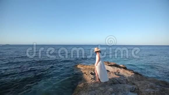 穿着白色连衣裙的漂亮女孩坐在海滩上希腊视频的预览图
