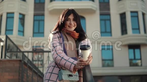 秋天城市背景下一位可爱的年轻女子的肖像一个穿秋装的女孩喝咖啡视频的预览图
