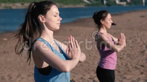两个女人站在城市河边的海滩上伸展瑜伽美丽的城市景色令人讨厌的姿势视频的预览图