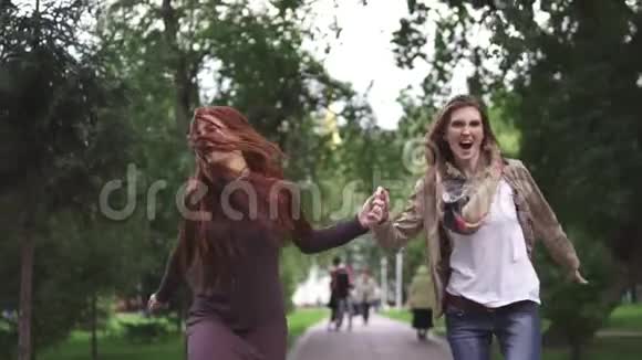 朋友们兴高采烈地穿过夏天的公园牵着手两个红色的女朋友跳着玩得开心玩得开心视频的预览图