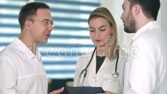 两位男医生正在讨论而微笑的护士在剪贴板上做笔记视频的预览图