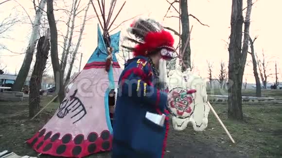 穿着全套衣服的北美印第安人一个穿着西装的印第安人在wigwam前面的街道上和一只手鼓跳舞视频的预览图