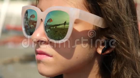 戴太阳镜的少女坐在海滩上用智能手机唱一首歌用耳机听她说话在里面视频的预览图